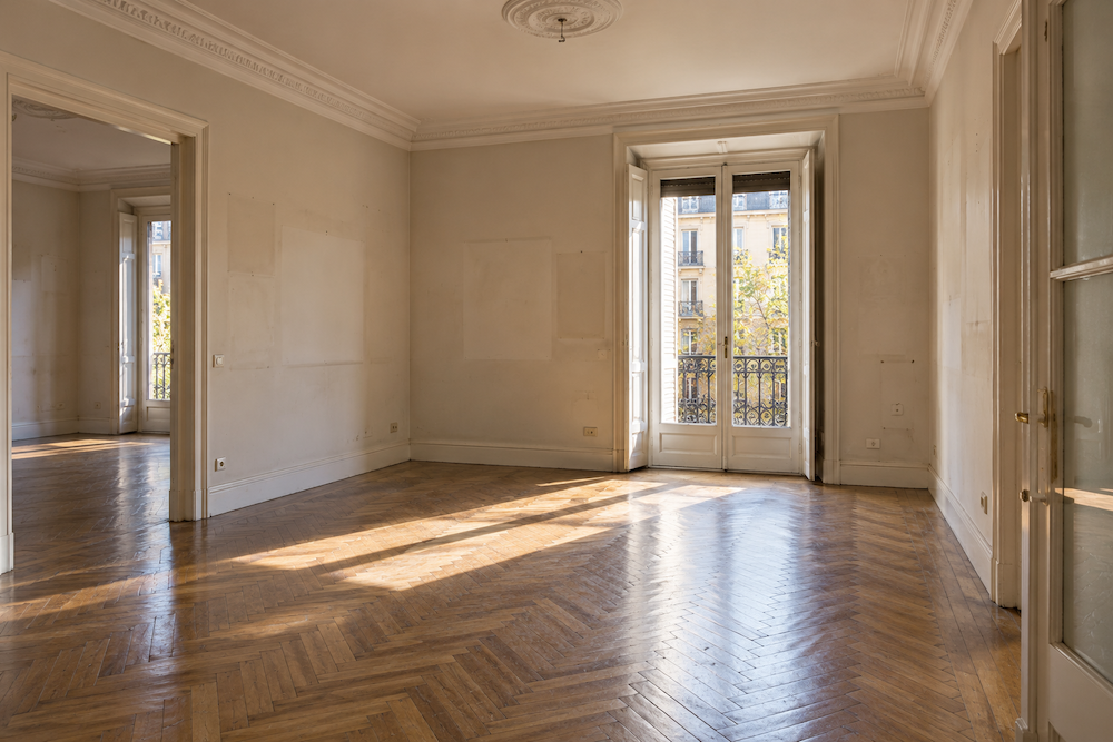 Salón vacío de una vivienda antigua con suelo de espiga y molduras tras el vaciado por herencia